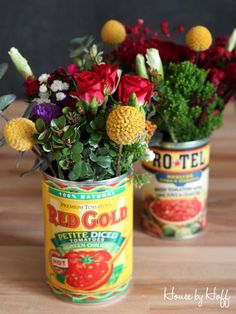 two tin cans filled with flowers on top of a wooden table