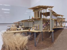 a model of a house made out of wooden planks and plywood boards on top of dry grass