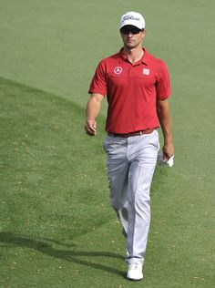 a man in red shirt and grey pants walking on green field with white ball cap