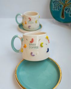 two coffee cups and saucers sitting on top of a blue plate with gold trim