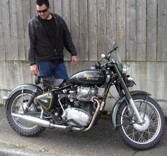 a man standing next to a motorcycle parked in front of a wooden fence on the street