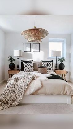 a bed with pillows and blankets on top of it next to two lamps hanging from the ceiling