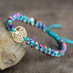 a bracelet with a gold tree charm on it and blue string around the clasp, sitting next to a rock