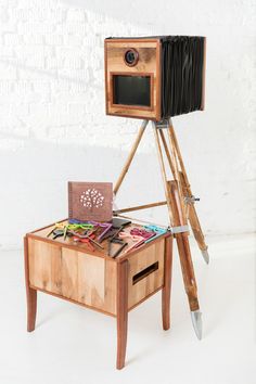 a wooden table topped with an old camera and lots of crafting supplies next to a white brick wall