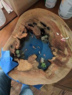 a wooden bowl filled with water on top of a table next to a person's feet