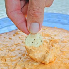 a hand dipping a cracker into a bowl of dippy cheese sauce with a blue plate in the background