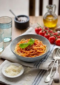 a bowl of spaghetti with tomato sauce and parmesan cheese next to some tomatoes