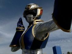 a man in a blue and gold suit holding up his hand to the sky while wearing a helmet