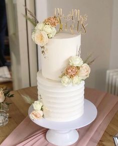 a white wedding cake with flowers and mr and mrs written on top is sitting on a table