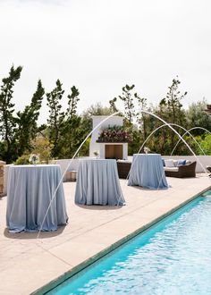 an outdoor dining set up next to a swimming pool with chairs and table cloths