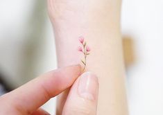 a small pink flower tattoo on the left side of her right arm, and behind her left hand is a tiny branch