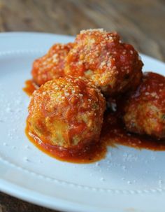 three meatballs covered in marinara sauce on a white plate with a wooden table