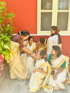 a group of women sitting next to each other in front of a red wall and potted plant