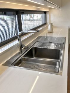 a stainless steel sink in a kitchen next to a window with blinds on the windowsill