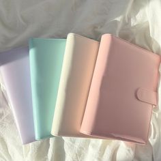 three different colored notebooks sitting on top of a white sheet covered bed with sheets