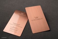 two metal business cards sitting on top of a gray cloth covered surface with the word monarch written in gold foil