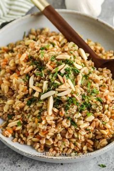 a white bowl filled with brown rice and chopped green herbs next to a wooden spoon