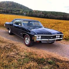 an old black car parked on the side of a road in front of a field