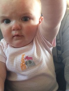 a baby sitting in a car seat with its hand up to her head and looking at the camera