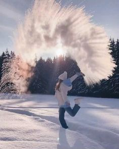 a woman is running through the snow with her arms in the air and trees behind her