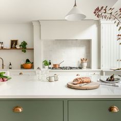 a kitchen with green cabinets and white counter tops, along with brass pulls on the cabinet doors