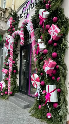 pink and white christmas decorations on the side of a building with candy canes hanging from it