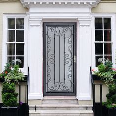 the front door to a house with potted plants on either side and windows above it