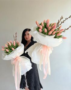 a woman holding two large bouquets of tulips in her hands, both wrapped in white paper and tied with pink ribbon