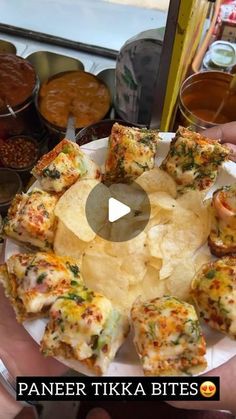 a person holding a plate full of food with chips and sauces in the background