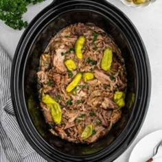 a slow cooker filled with meat and pickles on top of a white table