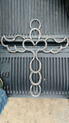 a cross made out of metal on top of a grilling grate next to someone's feet