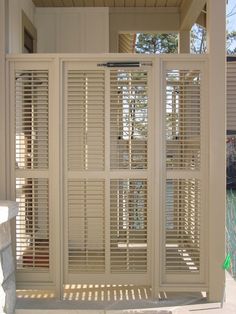 an open white door with shutters on the outside and inside, in front of a house