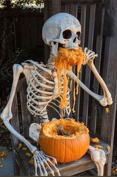 a skeleton sitting on top of a wooden bench eating something out of a pumpkin bowl