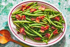 green beans with bacon in a white bowl next to a wooden spoon on a marble surface