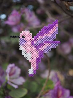 a pink and purple bird made out of perler beads hanging from a tree branch