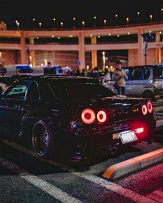 the back end of a black car parked in front of a parking lot at night