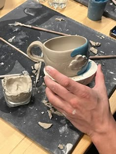 a person holding a cup on top of a table next to some paint and brushes