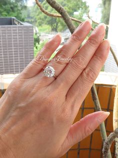 a woman's hand with a diamond ring on top of her finger, in front of a tree