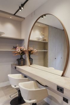 a mirror sitting on top of a counter next to two chairs and a vase with flowers