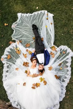 two people laying on top of an umbrella with leaves falling from it and one person wearing a white dress