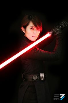 a woman holding a light saber in her right hand and wearing a black outfit with red lights