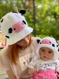 a woman holding a baby wearing a hat with two cows on it's side