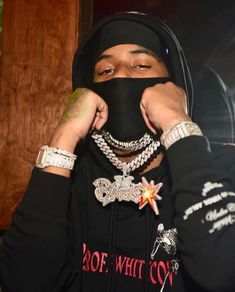 a young man wearing a black hoodie holding his face covered by chains and necklaces