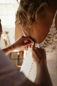 a woman helping another woman put on her wedding dress