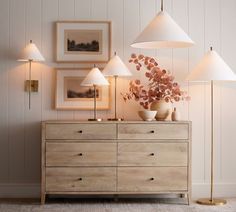 a dresser with three lamps on top and two pictures above it