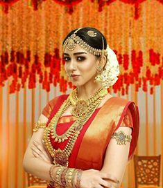 a woman in an orange and red sari with her arms crossed, wearing gold jewelry