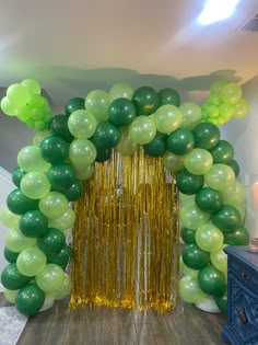 green and gold balloon arch with streamers on wood floor in front of white wall