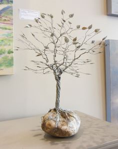 a metal tree with leaves and branches in a rock on a table next to a painting