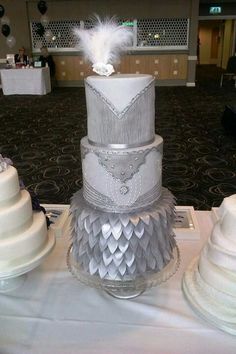 a three tiered wedding cake with feathers on top sits on a white tablecloth