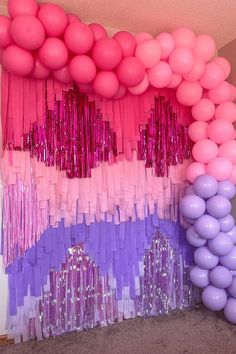 balloons and streamers are hanging from the ceiling in front of a purple, pink and white backdrop